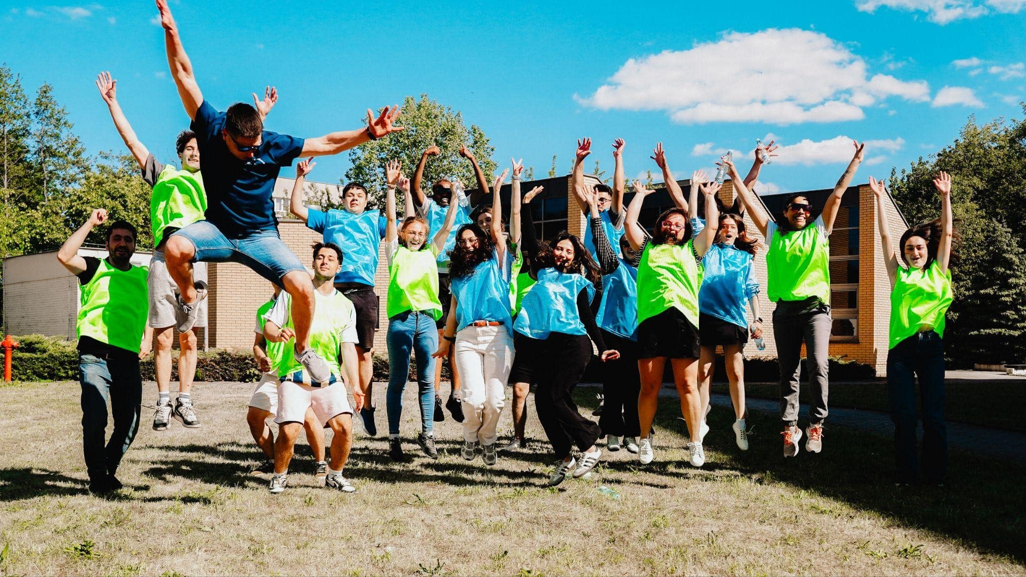 Zajęcia sportowe w ramach programu Erasmus+. Studenci w strojach sportowych skaczą wysoko do zdjęcia z uniesionymi w górę rękami.